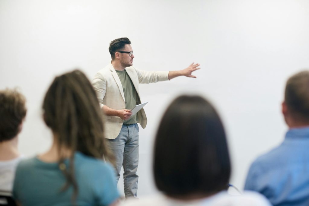 A man in a blazer gives a presentation to a captivated audience in a lecture setting.